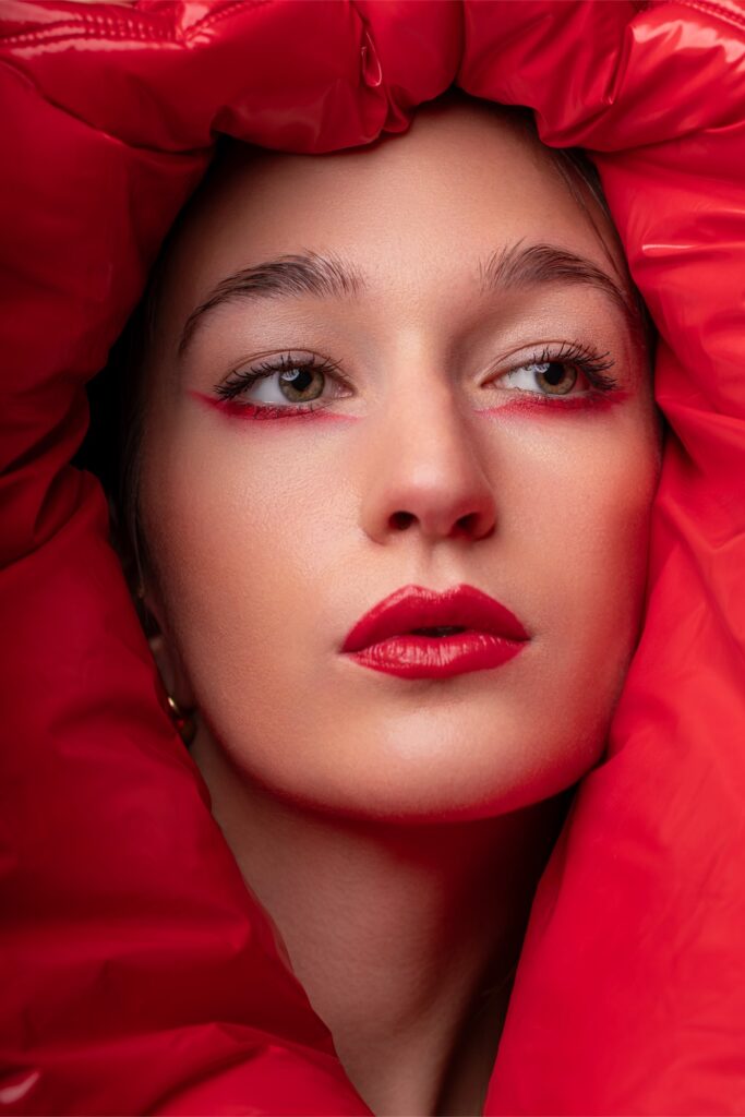 Portrait beauté d’une femme encadrée par un tissu rouge avec maquillage graphique