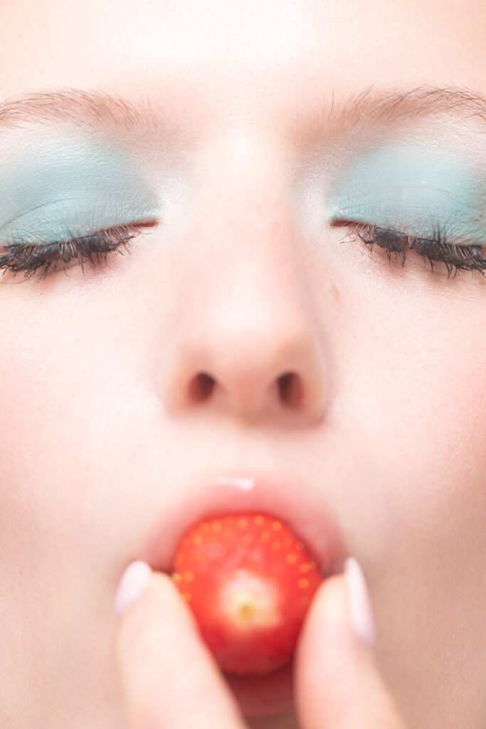 Portrait beauté créatif d’une femme aux yeux fermés tenant un fruit rouge près des lèvres