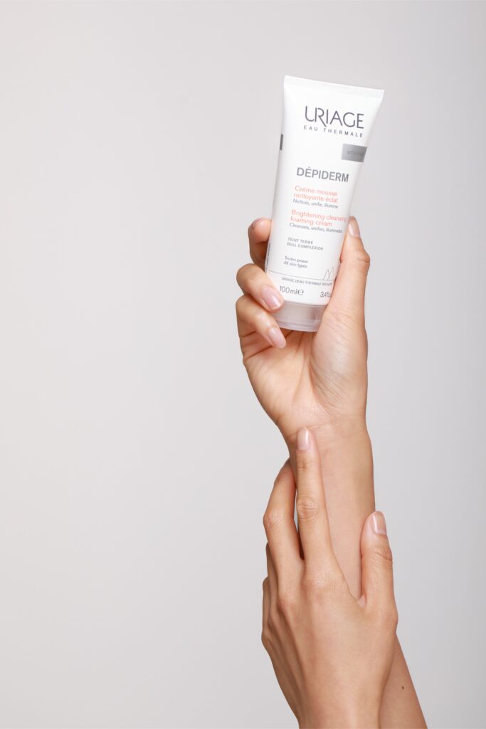 Main tenant un produit cosmétique Uriage sur fond neutre