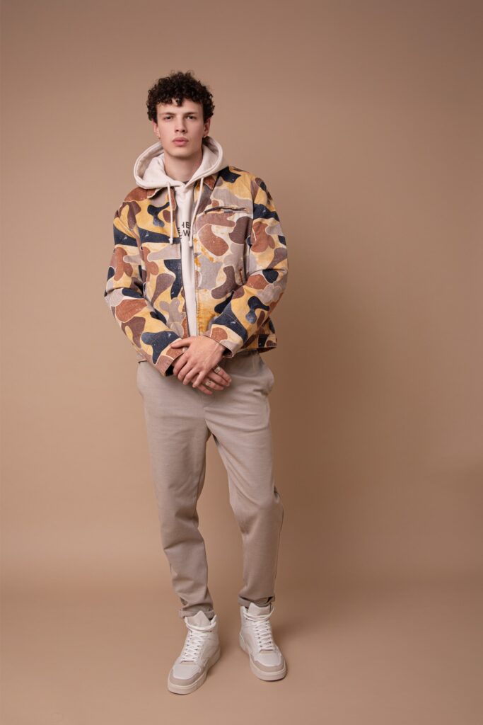 Modèle homme debout en studio, tenue streetwear beige avec veste imprimée, silhouette contemporaine