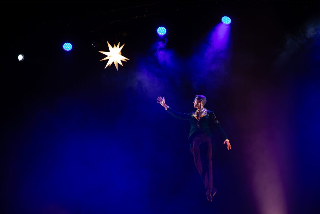 Artiste illusionniste en apesanteur sur scène avec éclairage bleu et violet, photographie de spectacle à Lyon