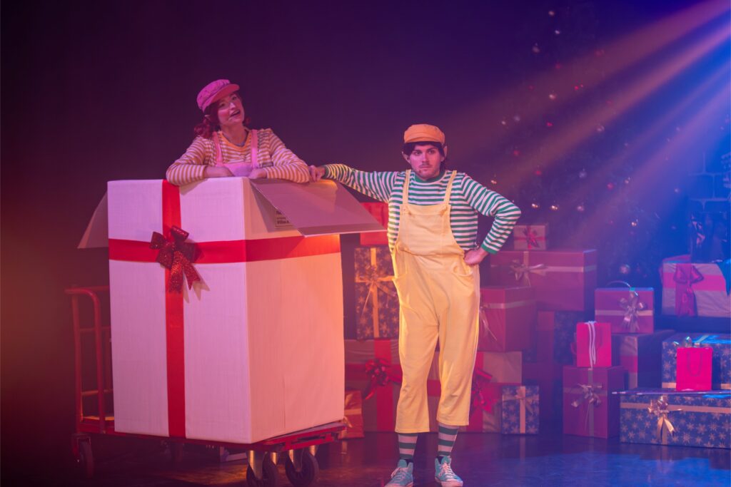 Artistes sur scène dans un décor de Noël avec cadeaux et éclairage coloré, photographie de spectacle à Lyon